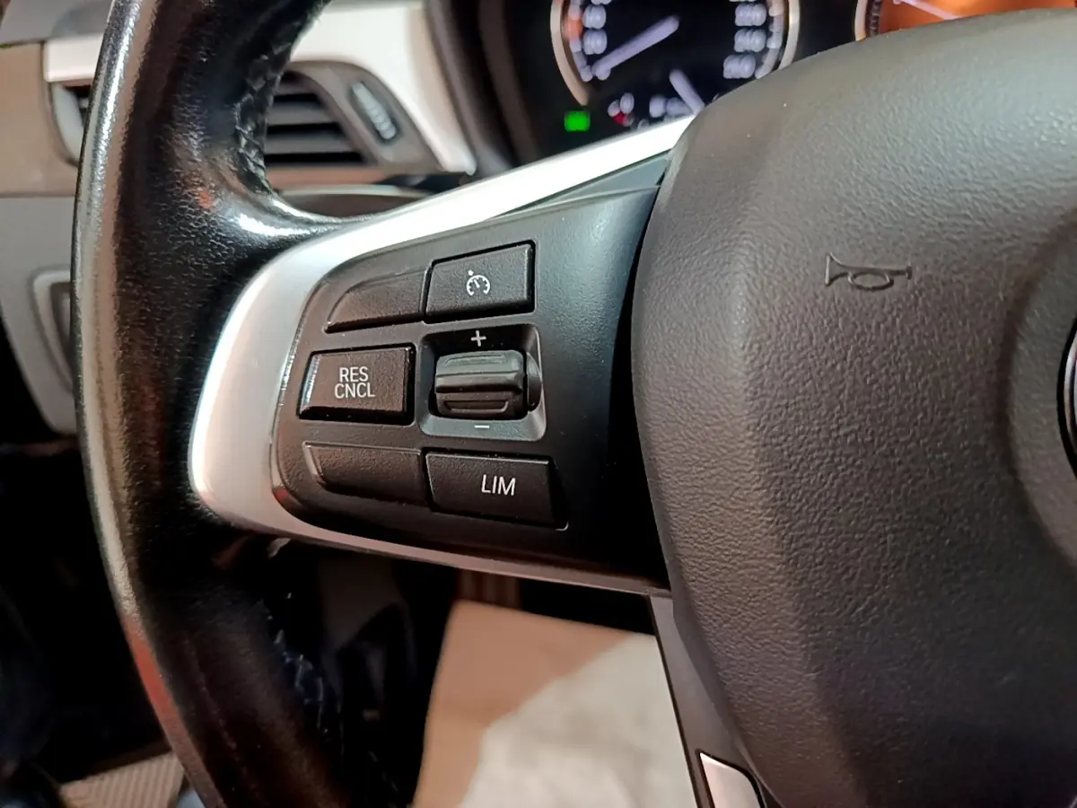 Gros plan sur les commandes de régulateur de vitesse du volant cuir noir de la BMW X1 sDrive16d 2020.