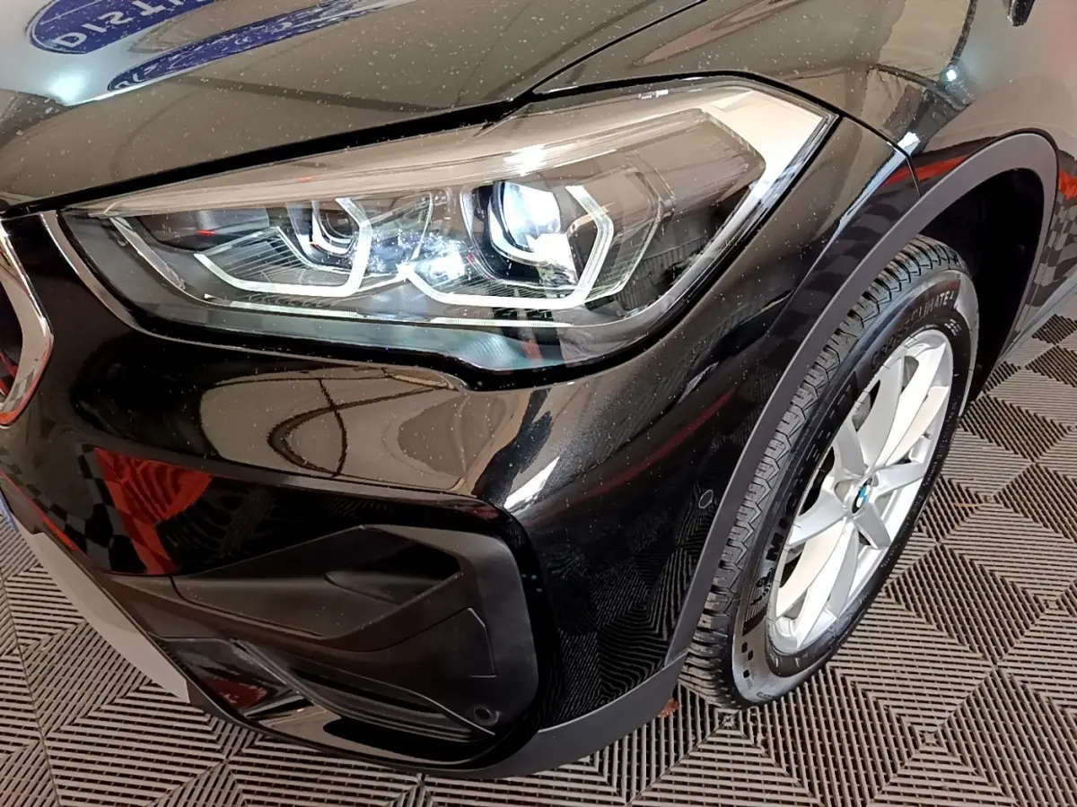Gros plan sur le phare avant gauche et la roue d’une BMW X1 noire, mettant en valeur les détails modernes du design.