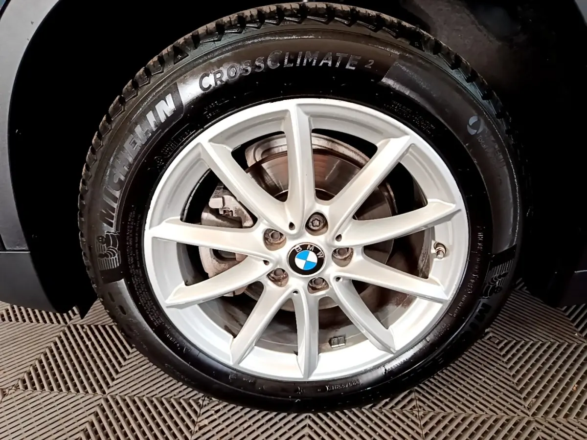 Gros plan sur la roue avant gauche noire d’un BMW X1 2020 avec jante alliage argentée et logo BMW central.