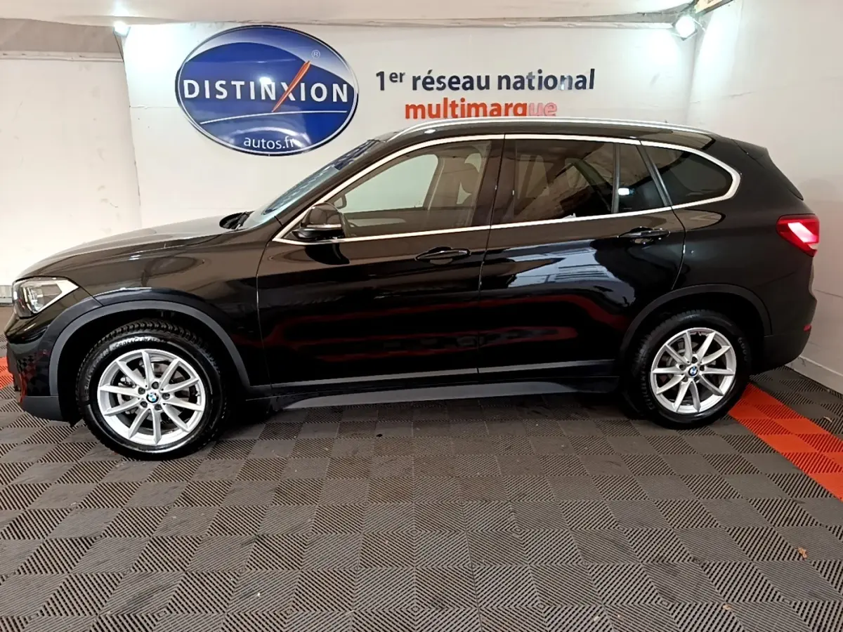 Profil côté gauche d'un BMW X1 noir 2020, finition Business Design, sur sol damier en intérieur showroom.