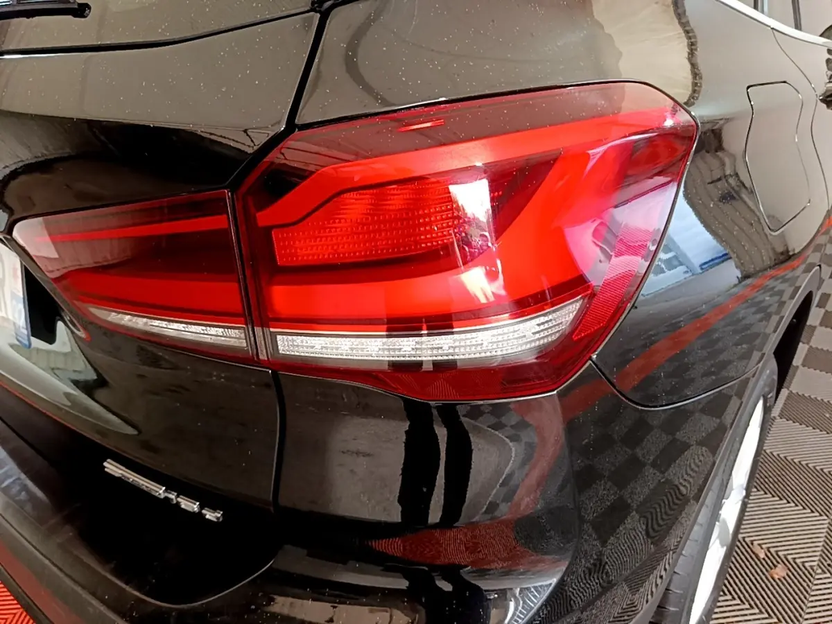 Gros plan sur le feu arrière droit d’un BMW X1 noir, mettant en valeur la finition brillante et les lignes du coffre arrière.