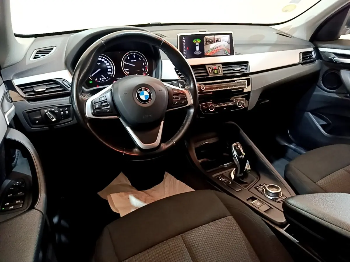 Intérieur noir de BMW X1 2020 vu côté conducteur, volant cuir multifonctions et écran tactile 8,8 pouces affichant caméra de recul.