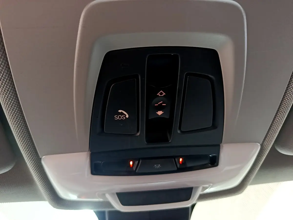 Panneau de commandes au plafond avec bouton SOS et éclairage intérieur activé dans une BMW X1 noire de 2020.