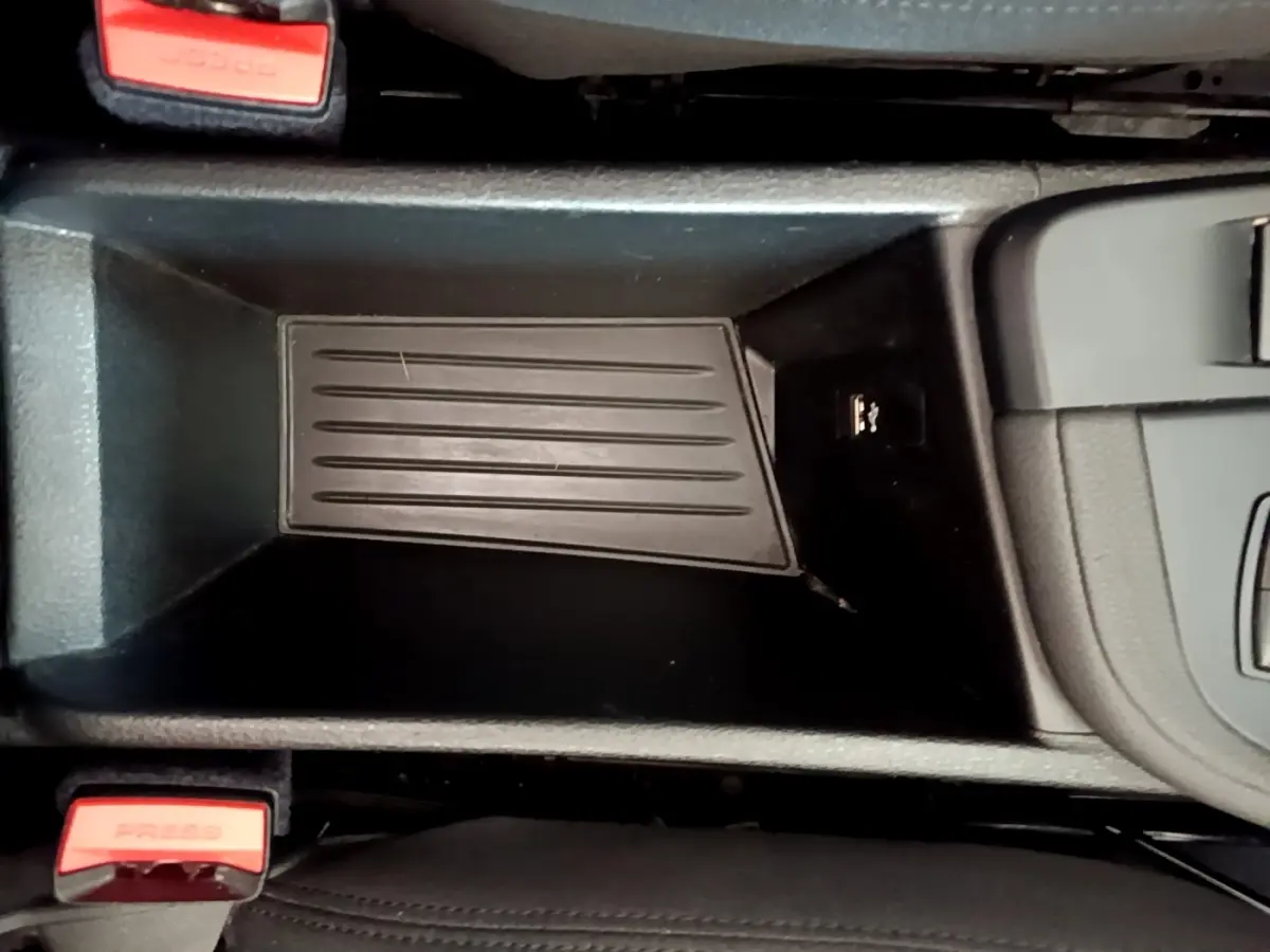 Gros plan sur le rangement central noir du BMW X1 sDrive16d Business Design avec prises USB et boutons de ceinture rouge.