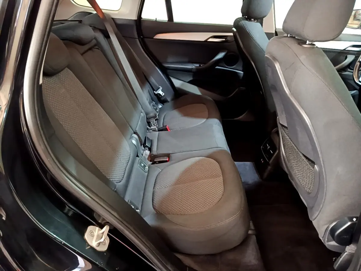 Vue intérieure côté gauche sur la banquette arrière noire du BMW X1 sDrive16d Business Design 2020.