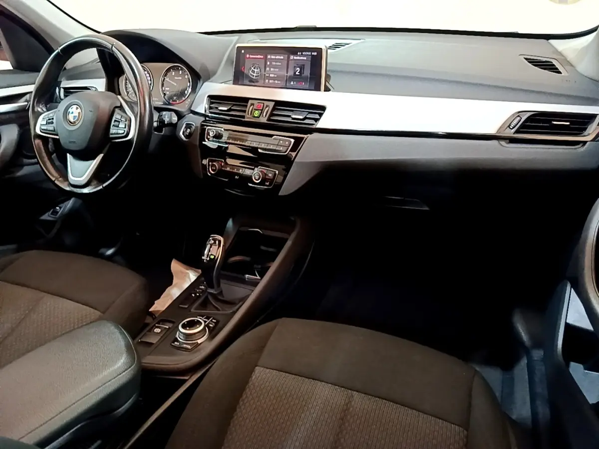 Intérieur BMW X1 sDrive16d 2020 vu côté conducteur, tableau de bord noir avec écran tactile 8,8 pouces et volant cuir.