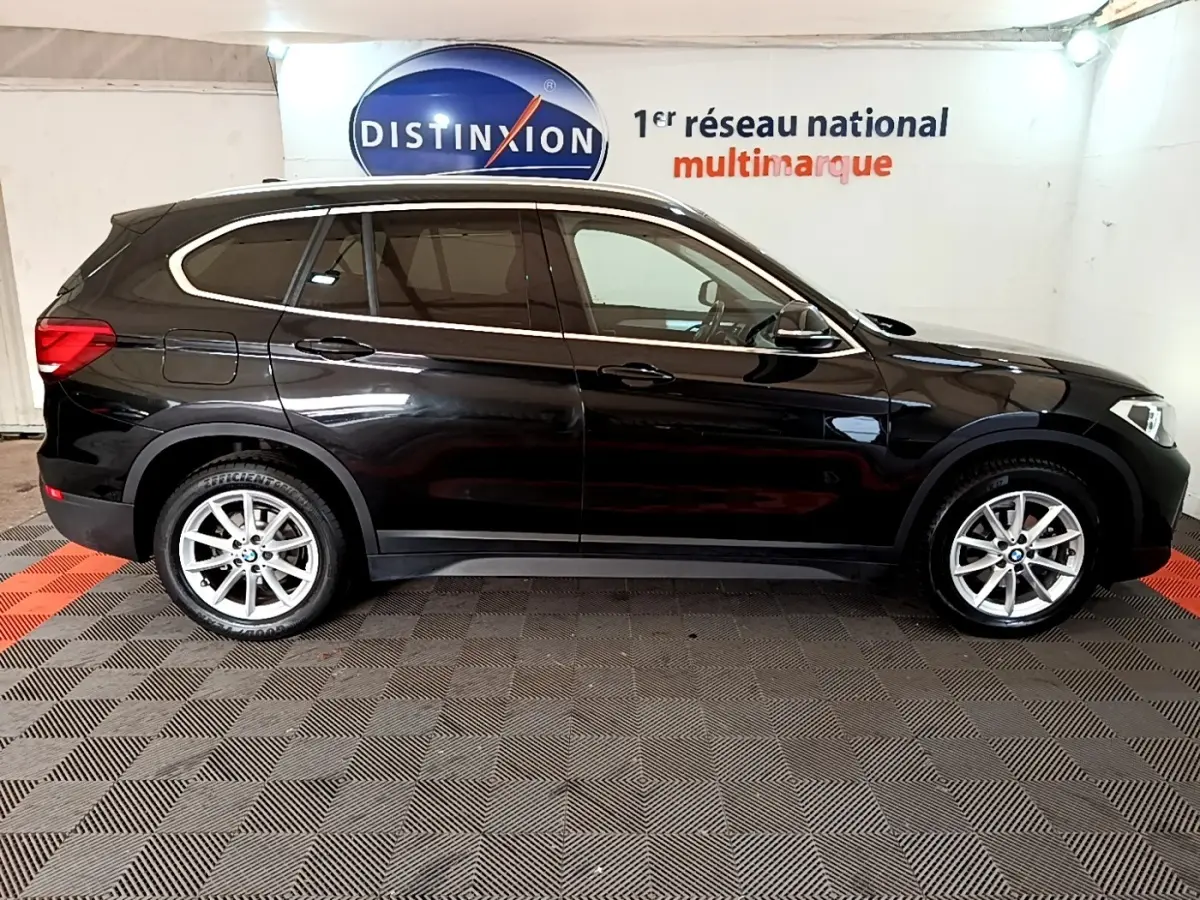 Profil droit d'un BMW X1 noir 2020 garé en intérieur, soulignant ses lignes élégantes et ses jantes argentées.