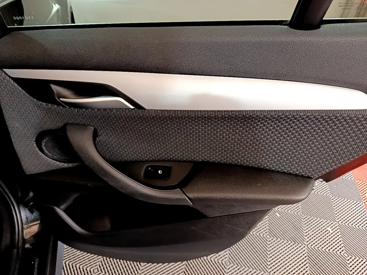 Détail de la porte intérieure côté gauche du BMW X1 noir, avec poignée argentée et bouton de verrouillage.