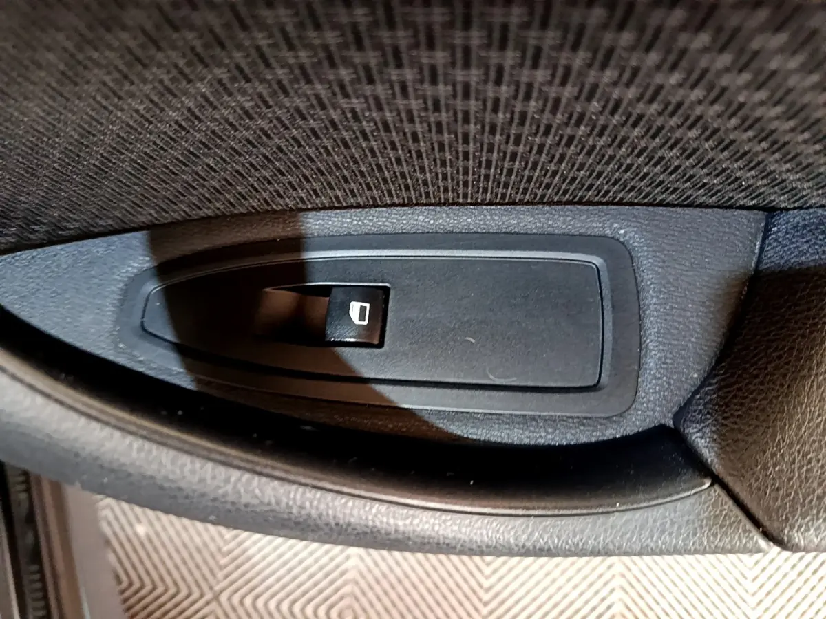 Gros plan sur le bouton de commande de lève-vitre côté conducteur du BMW X1 noir sDrive16d Business Design 2020.