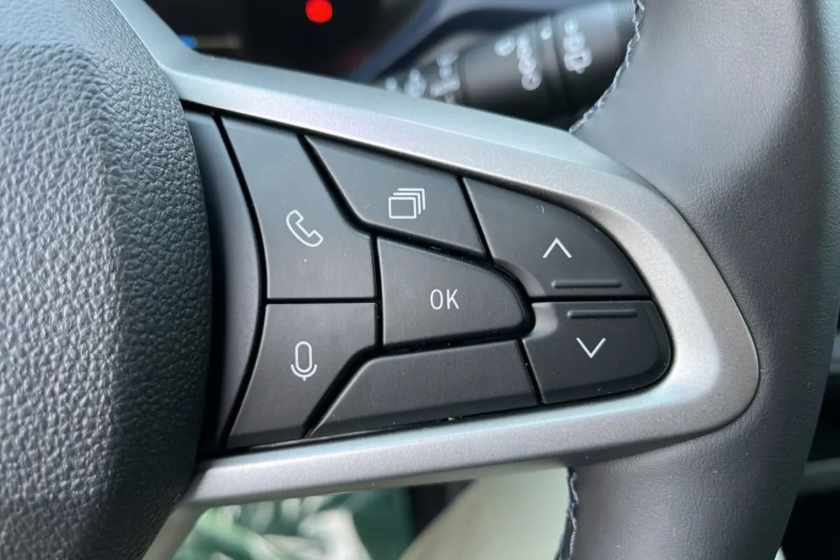 Gros plan sur les commandes noires du volant cuir gris du Dacia Bigster Hybrid 155 Expression Plus, boutons multifonctions visibles.