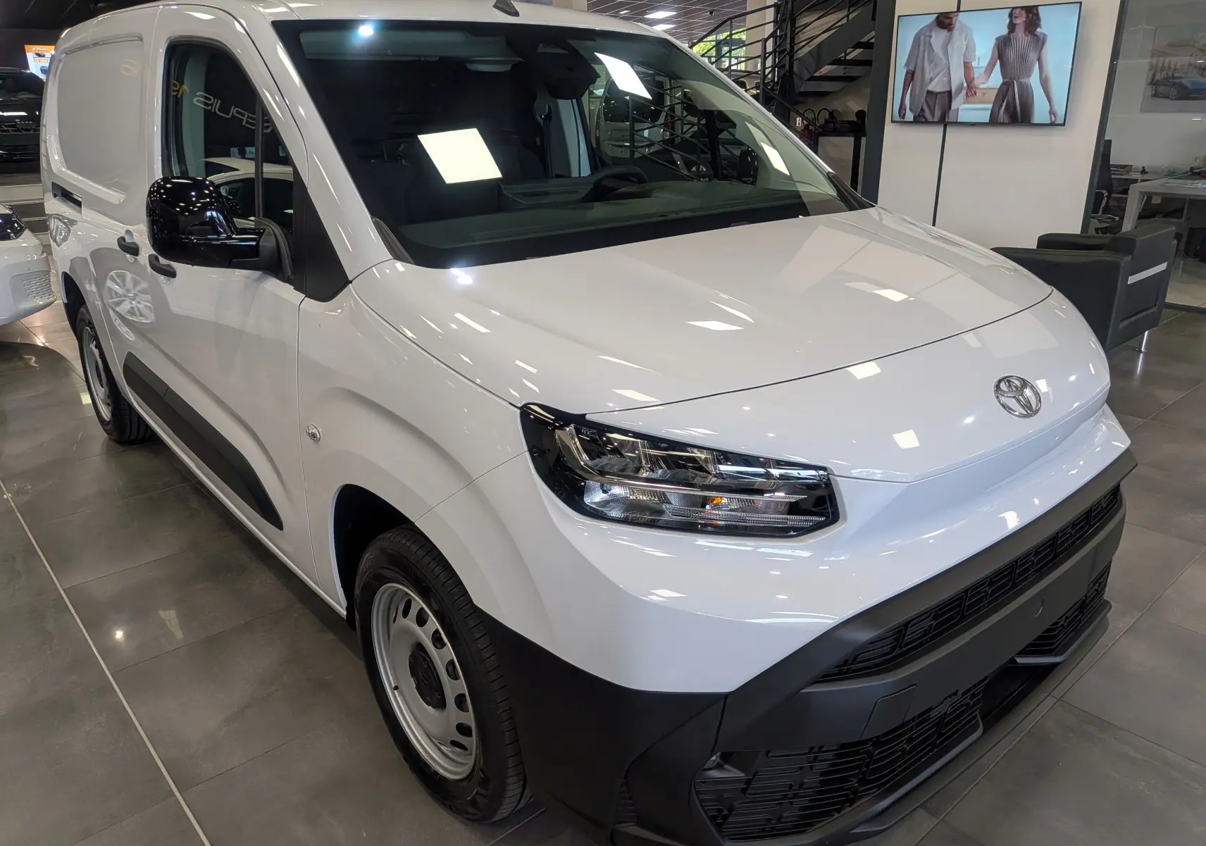 Toyota Proace City Long blanc glacier vue 3/4 avant droit en intérieur avec détails noirs contrastants sur pare-chocs et rétroviseurs.