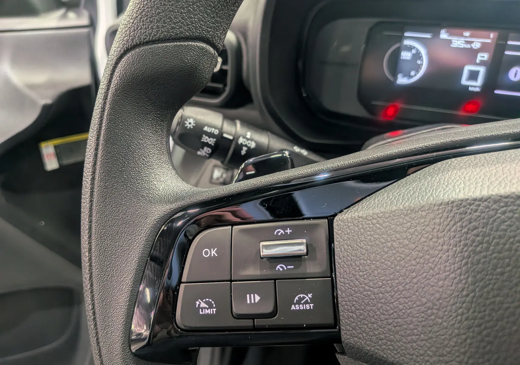Gros plan sur les commandes au volant noir du Toyota Proace City blanc, avec tableau de bord numérique en arrière-plan.