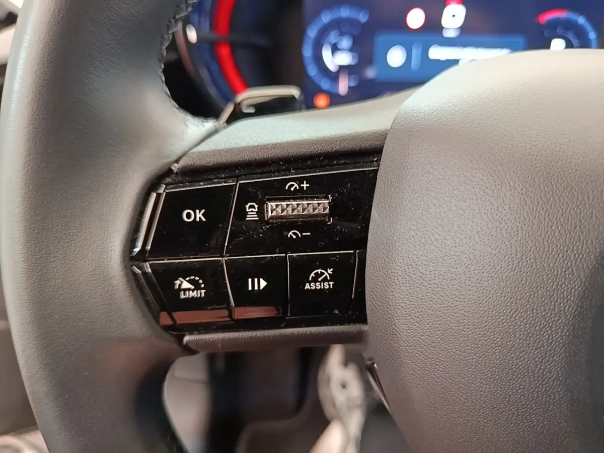 Gros plan sur le côté gauche du volant cuir noir de l'Alfa Romeo Junior 2024, avec commandes multifonctions et tableau de bord flou.