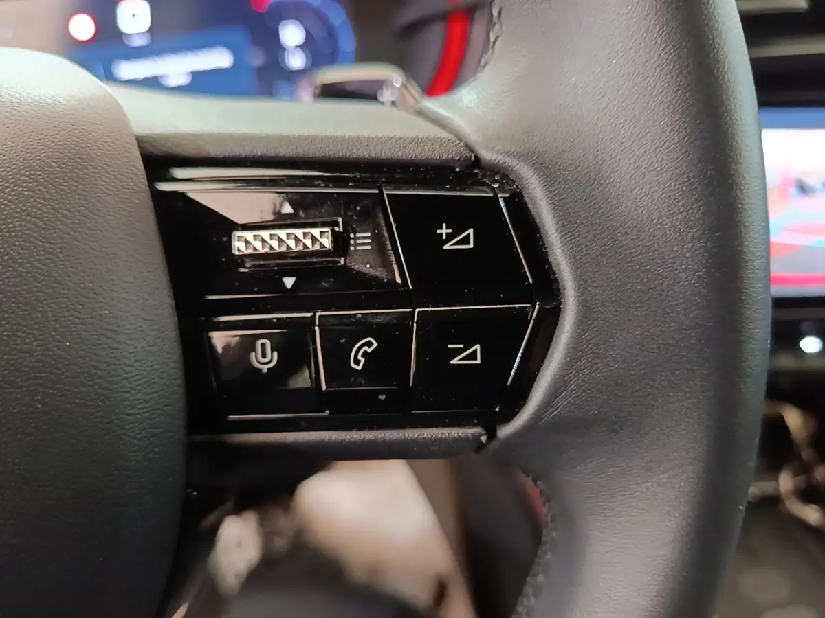 Gros plan sur les commandes noires du volant cuir de l'Alfa Romeo Junior 1.2 Ibrida 2024, avec boutons multifonctions.