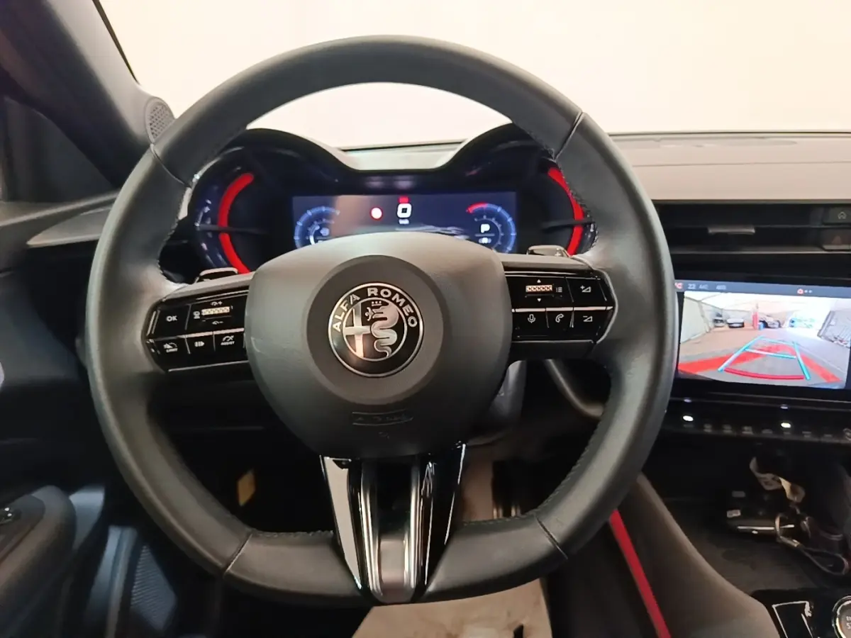 Vue intérieure centrée sur le volant cuir noir d'Alfa Romeo Junior 2024 avec tableau de bord numérique et écran de recul.