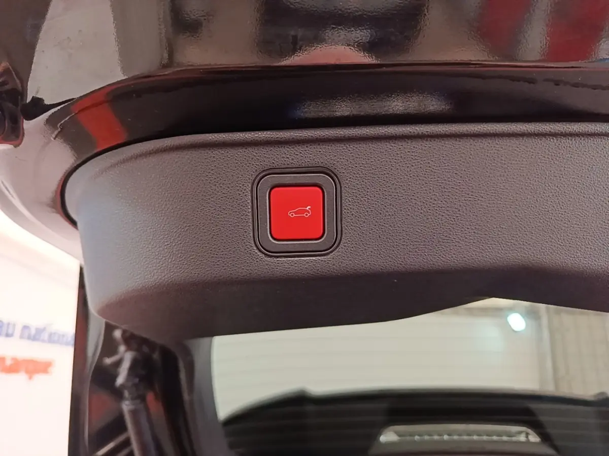 Gros plan sur le bouton rouge d'ouverture électrique du coffre, sur la partie intérieure du hayon noir d'une Alfa Romeo Junior 2024.