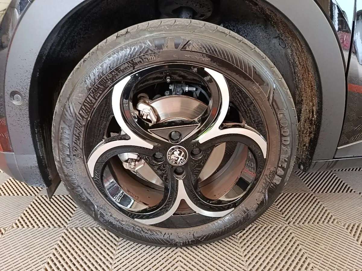 Gros plan sur la roue avant droite noire d'une Alfa Romeo Junior 1.2 Ibrida 136ch Speciale DCT6 avec jante bi-ton distinctive.