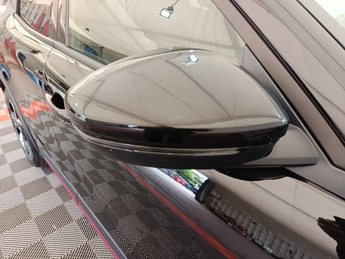 Rétroviseur côté gauche noir brillant d'une Alfa Romeo Junior 2024, avec reflet de l'environnement intérieur.
