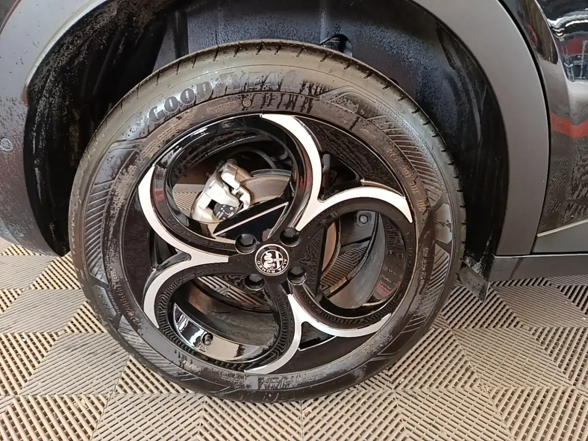 Gros plan sur la roue avant gauche noire de l'Alfa Romeo Junior 1.2 Ibrida 136ch Speciale DCT6 2024.