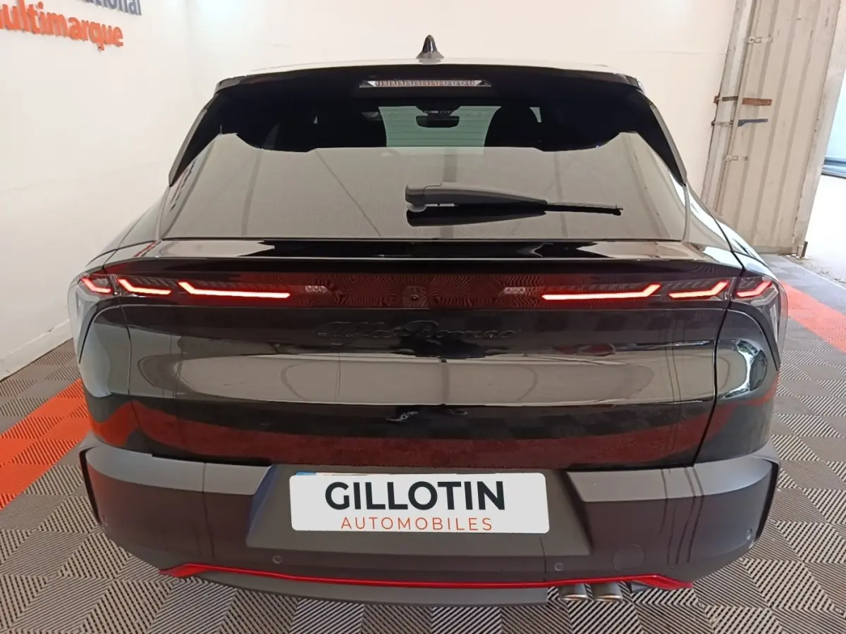 Vue arrière d’une Alfa Romeo Junior noire 2024 avec feux LED fins et double sortie d’échappement visible à droite.