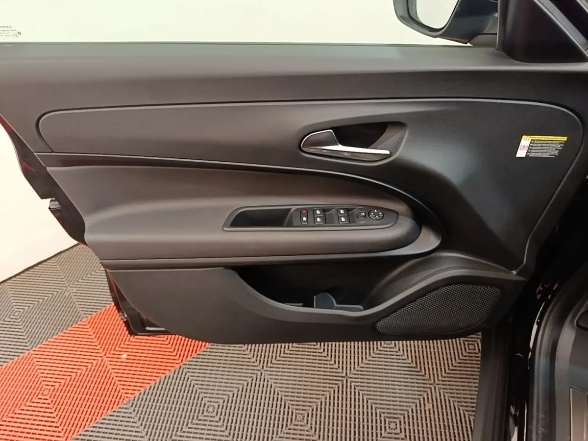 Vue rapprochée de la porte avant gauche noire de l'Alfa Romeo Junior 2024 avec commandes électriques et poignée argentée.