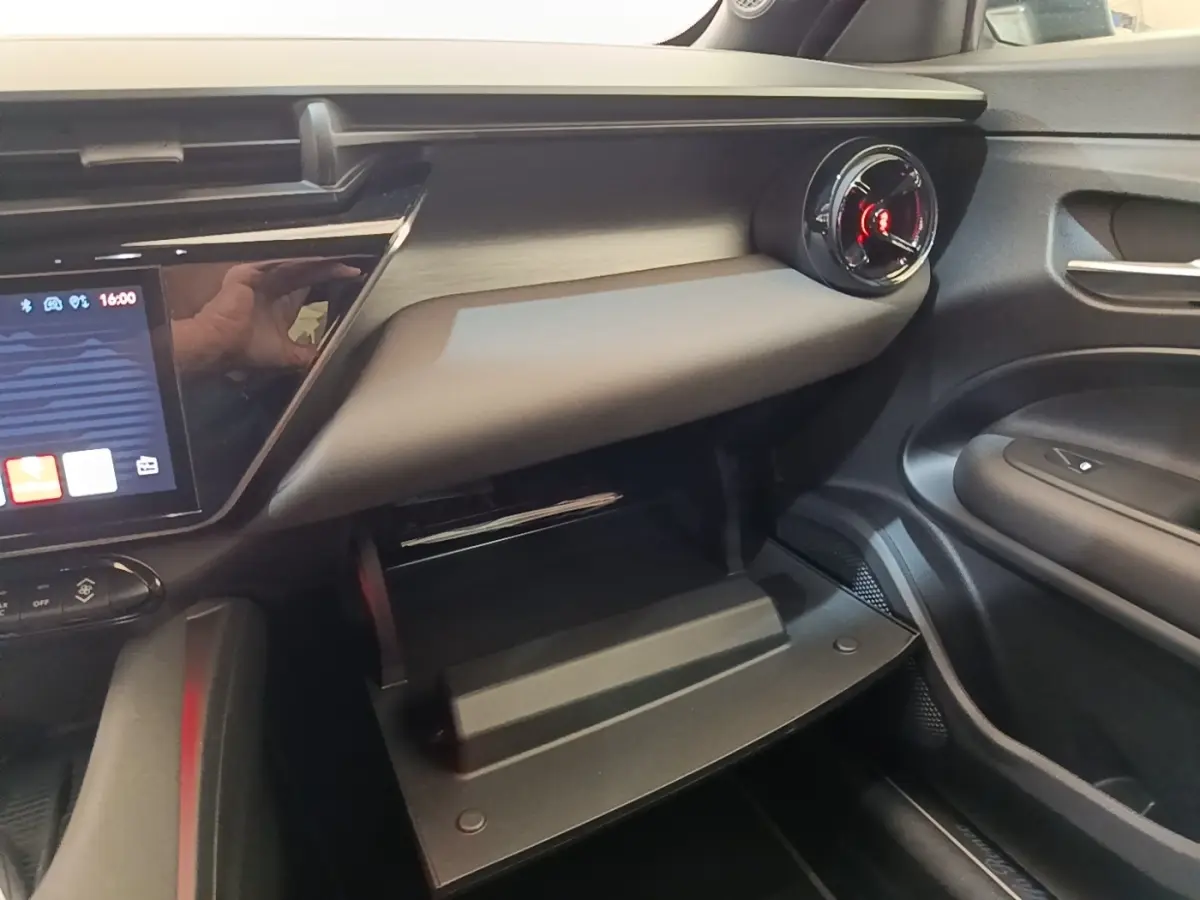 Intérieur côté passager de l'Alfa Romeo Junior 2024 noir, avec boîte à gants ouverte et aérateur rond rouge.