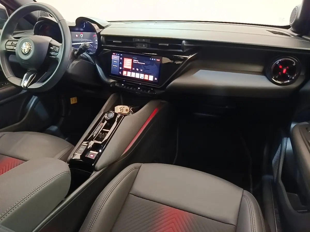 Vue intérieure côté conducteur de l'Alfa Romeo Junior 2024, tableau de bord noir avec écran tactile et volant cuir multifonctions.