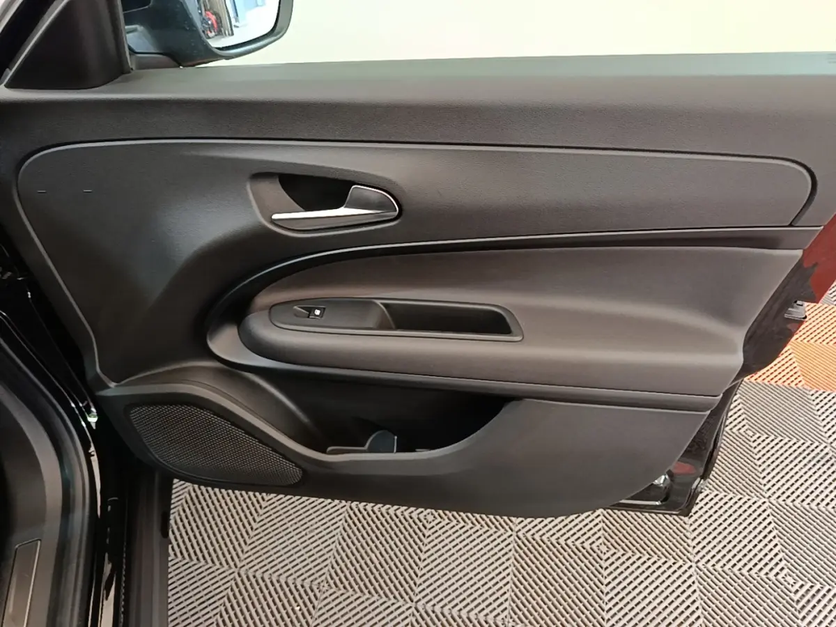 Vue intérieure du panneau de porte côté gauche noir de l'Alfa Romeo Junior 2024 avec poignée argentée et haut-parleur intégré.