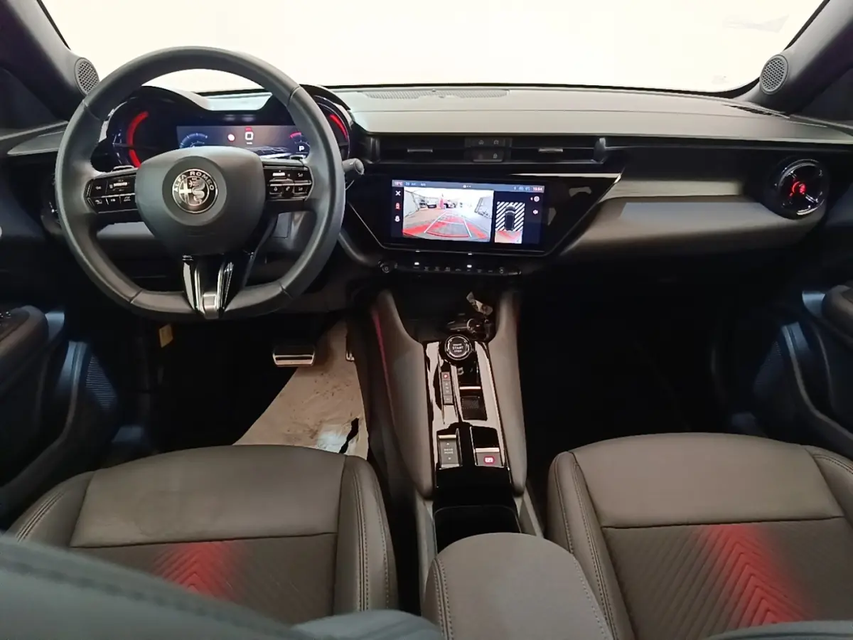 Vue intérieure avant de l'Alfa Romeo Junior 2024, tableau de bord noir avec écran tactile et volant cuir multifonctions.