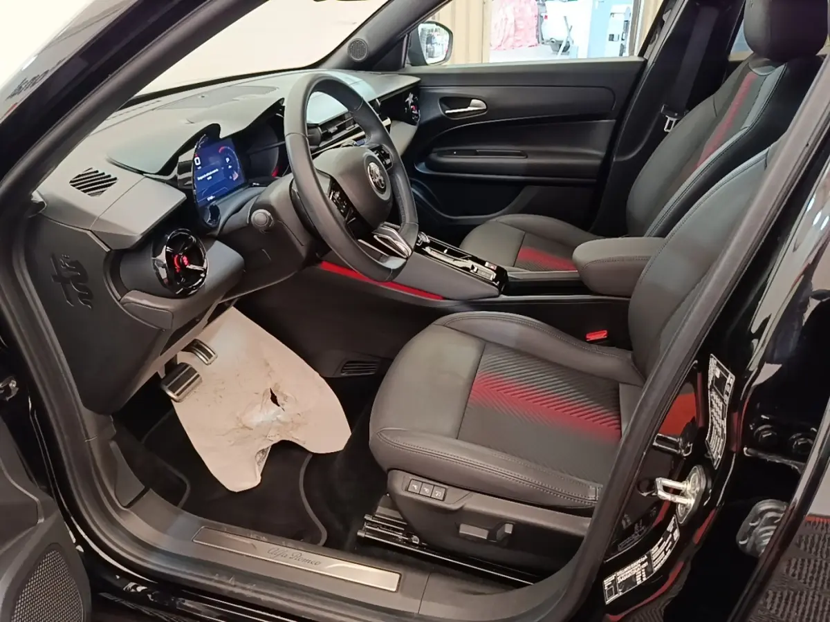 Vue intérieure côté conducteur de l'Alfa Romeo Junior 1.2 Ibrida noire, avec sièges en cuir et tableau de bord digital.