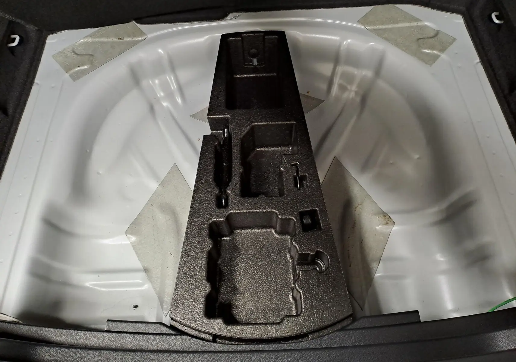 Coffre ouvert du Skoda Karoq blanc lune 2025, vue plongeante sur le rangement pour roue de secours et outils.