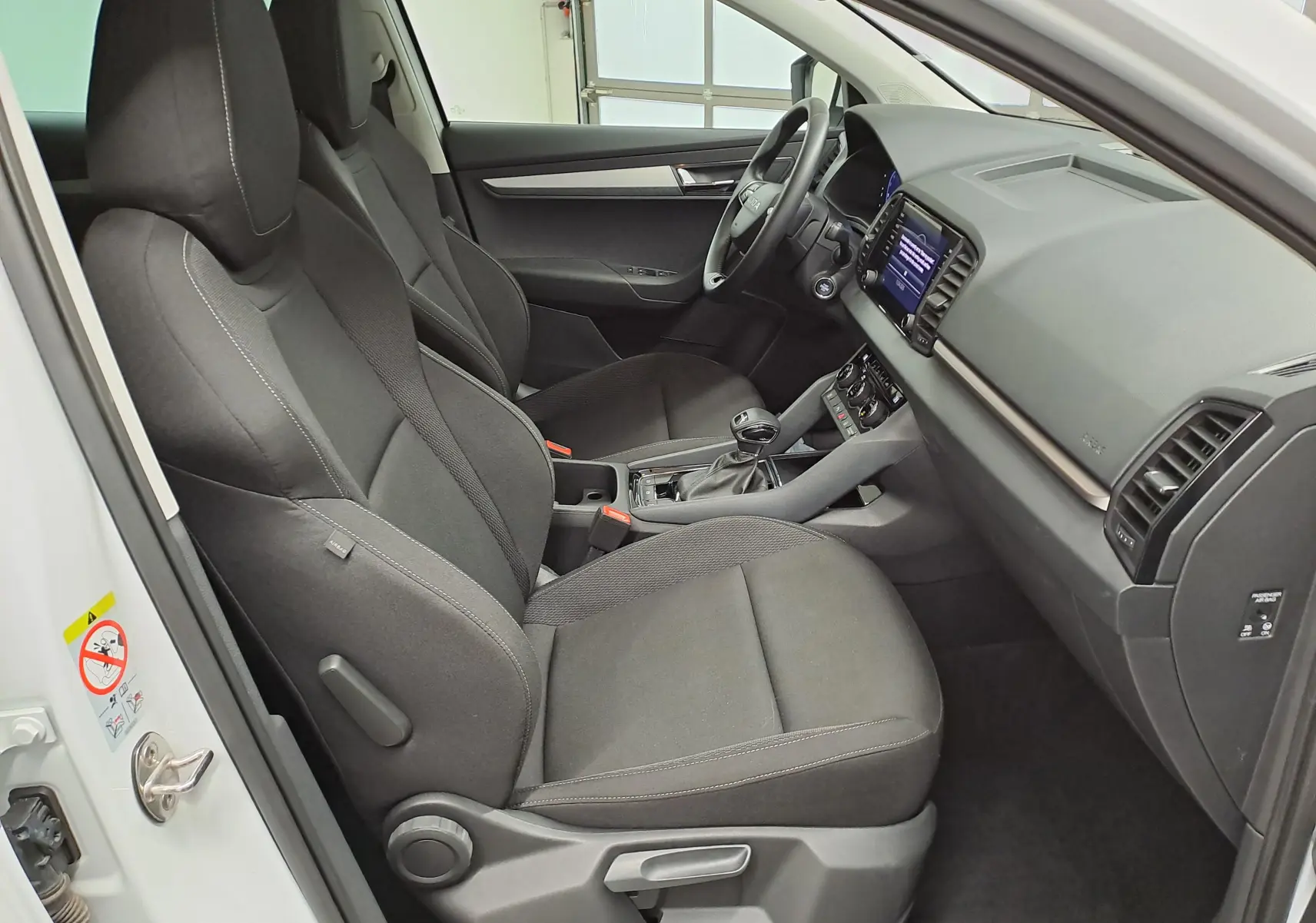 Vue intérieure côté conducteur du Skoda Karoq blanc lune 2025, montrant les sièges noirs et le tableau de bord moderne.