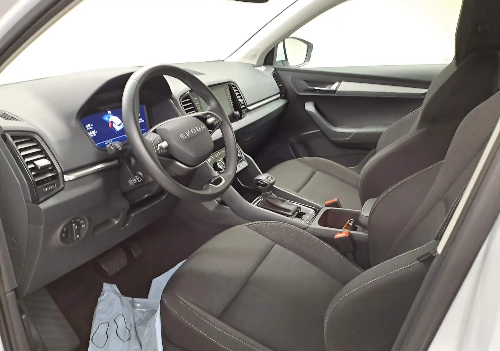 Intérieur avant droit du Skoda Karoq 2025 blanc lune, montrant le tableau de bord numérique et les sièges tissu noirs.