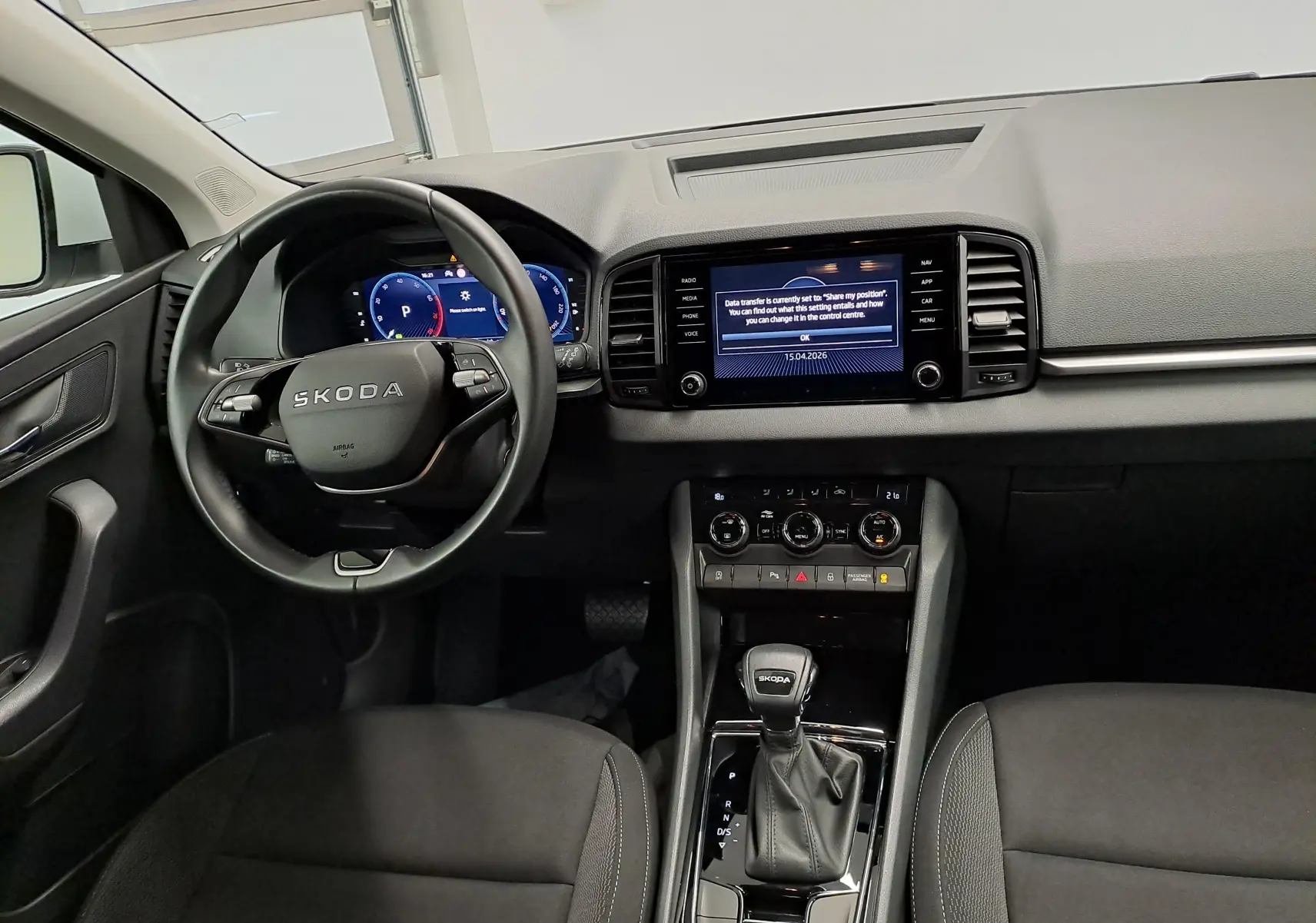 Vue intérieure avant du Skoda Karoq 2025, tableau de bord et volant noirs avec écran tactile central allumé.