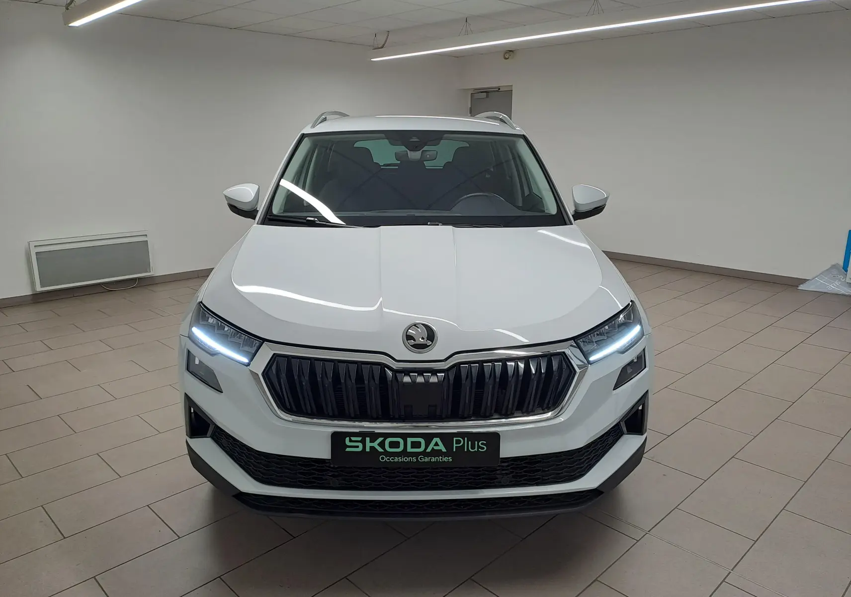 Vue frontale d'un Skoda Karoq blanc lune 2025 avec phares LED allumés et calandre noire distinctive.