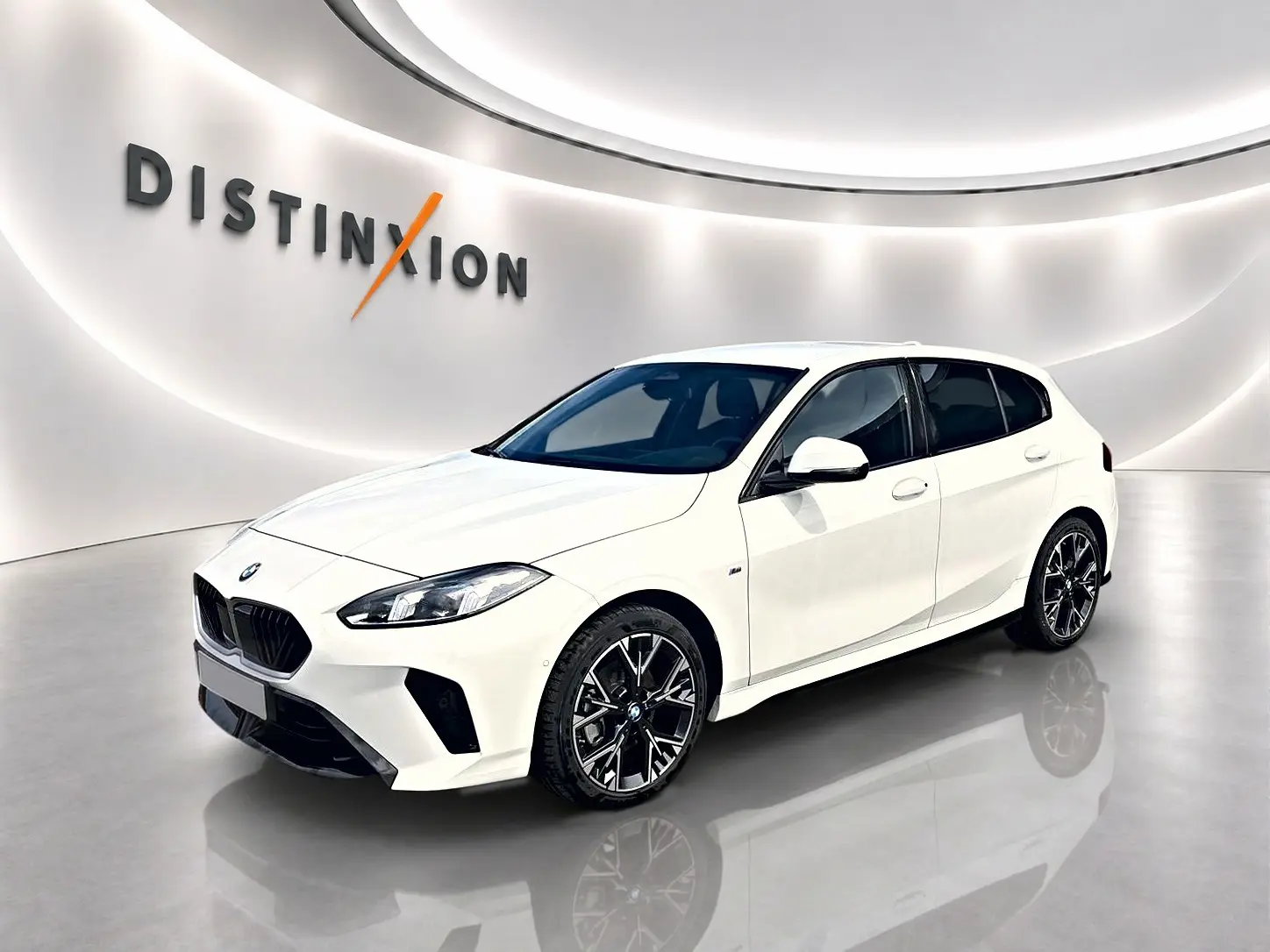 BMW Série 1 blanche vue en 3/4 avant droit, avec jantes alliage noires et calandre M sport dans un showroom lumineux.