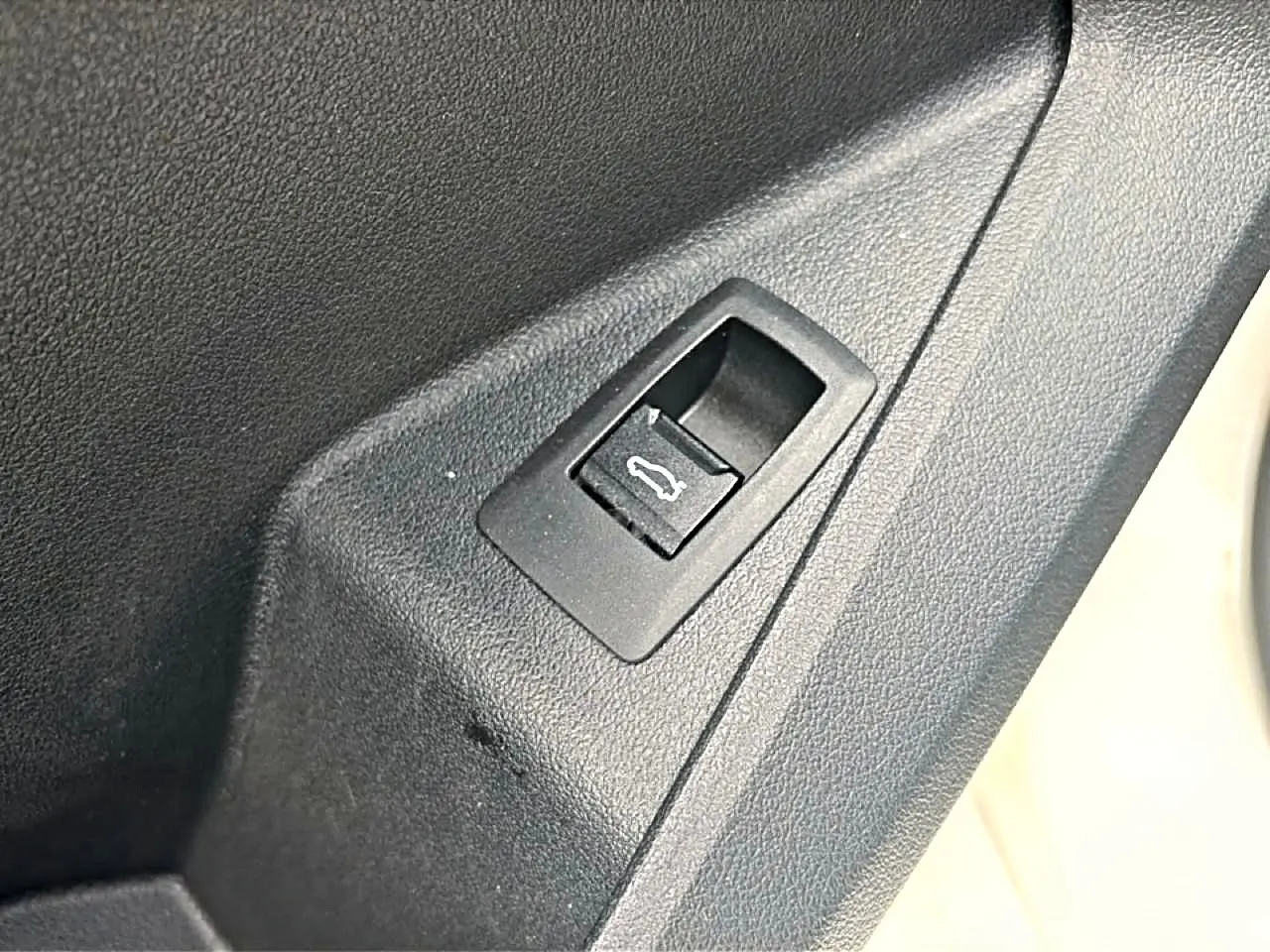 Gros plan sur le bouton d'ouverture du coffre dans l'habitacle d'une BMW Série 1 blanche.