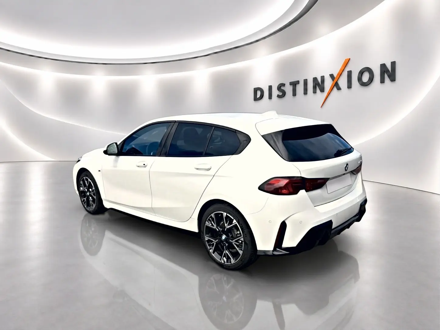 BMW Série 1 blanche vue en 3/4 arrière droit dans un showroom avec jantes alu noires et vitres teintées.