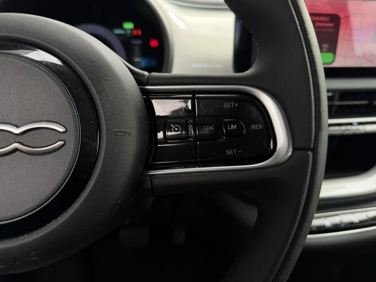 Gros plan sur le côté droit du volant noir Soft-Touch de la FIAT 500 électrique blanche, avec commandes de régulateur de vitesse.