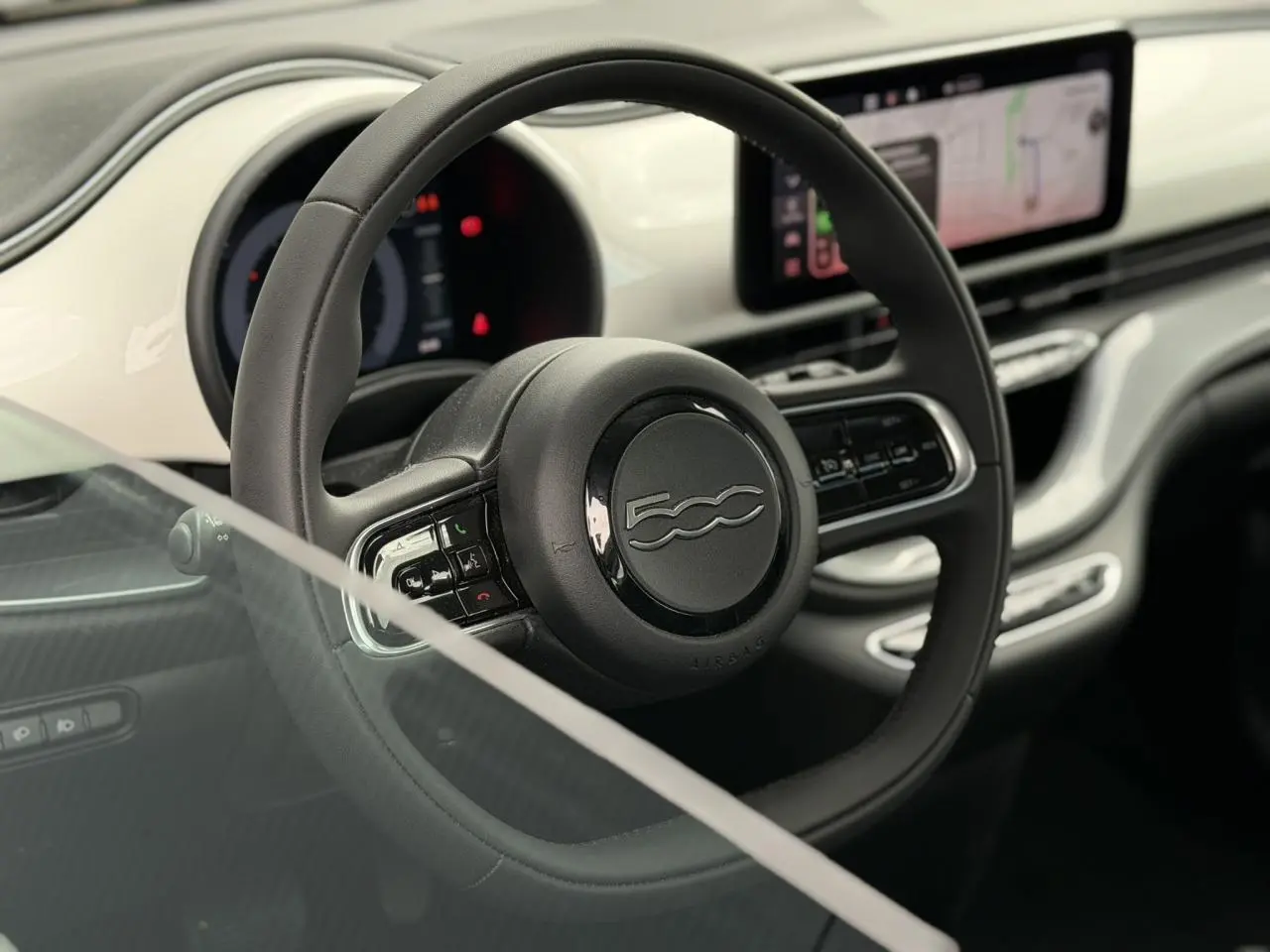 Vue rapprochée du volant noir Soft-Touch et du tableau de bord blanc Artic avec écran tactile du Fiat 500 électrique 2024.
