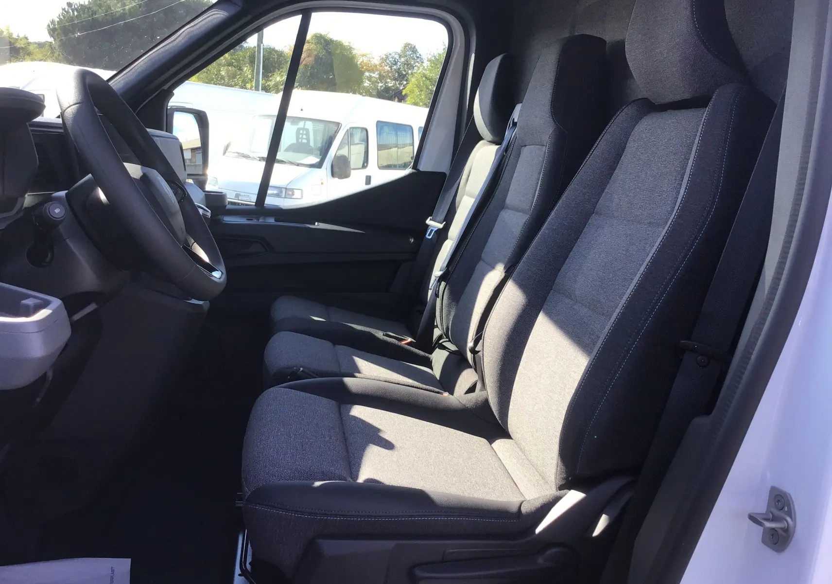 Intérieur côté conducteur du Renault Master blanc 2025, montrant les sièges gris et le volant à gauche.