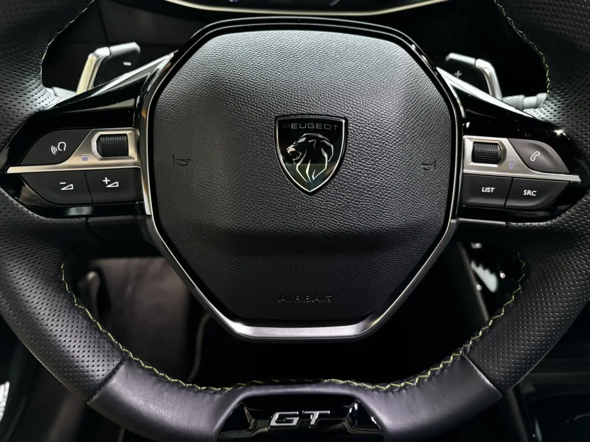 Gros plan sur le volant cuir noir perforé avec logo Peugeot et sigle GT de la 208 Hybrid 136 eDCS6 GT.