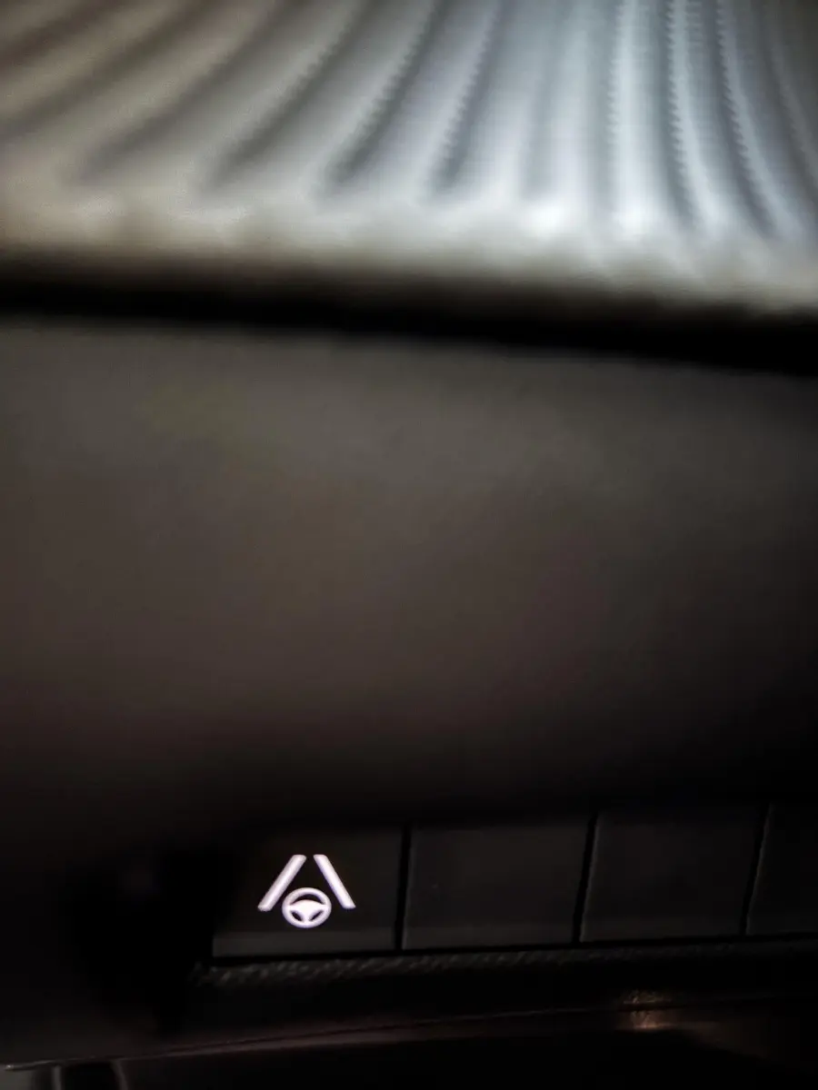 Gros plan sur le bouton d'assistance au maintien de voie dans l'habitacle sombre d'une Peugeot 208 Hybrid 136 eDCS6 GT gris foncé 2024.