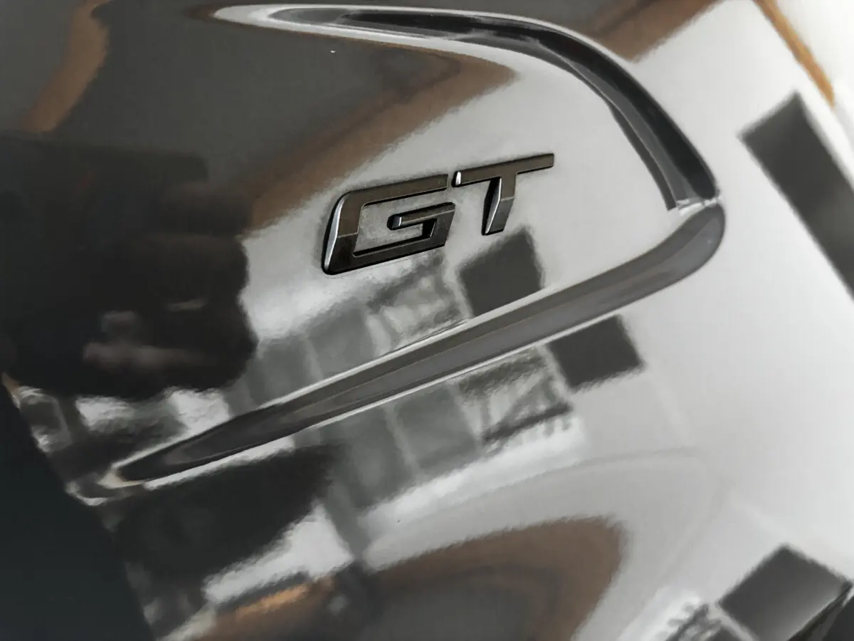 Gros plan sur l'emblème GT noir brillant sur la carrosserie gris foncé d'une Peugeot 208 Hybrid 136 eDCS6 GT.