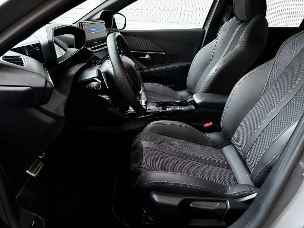 Intérieur avant droit de la Peugeot 208 Hybrid 136 eDCS6 GT 2024 avec sièges gris et tableau de bord numérique.