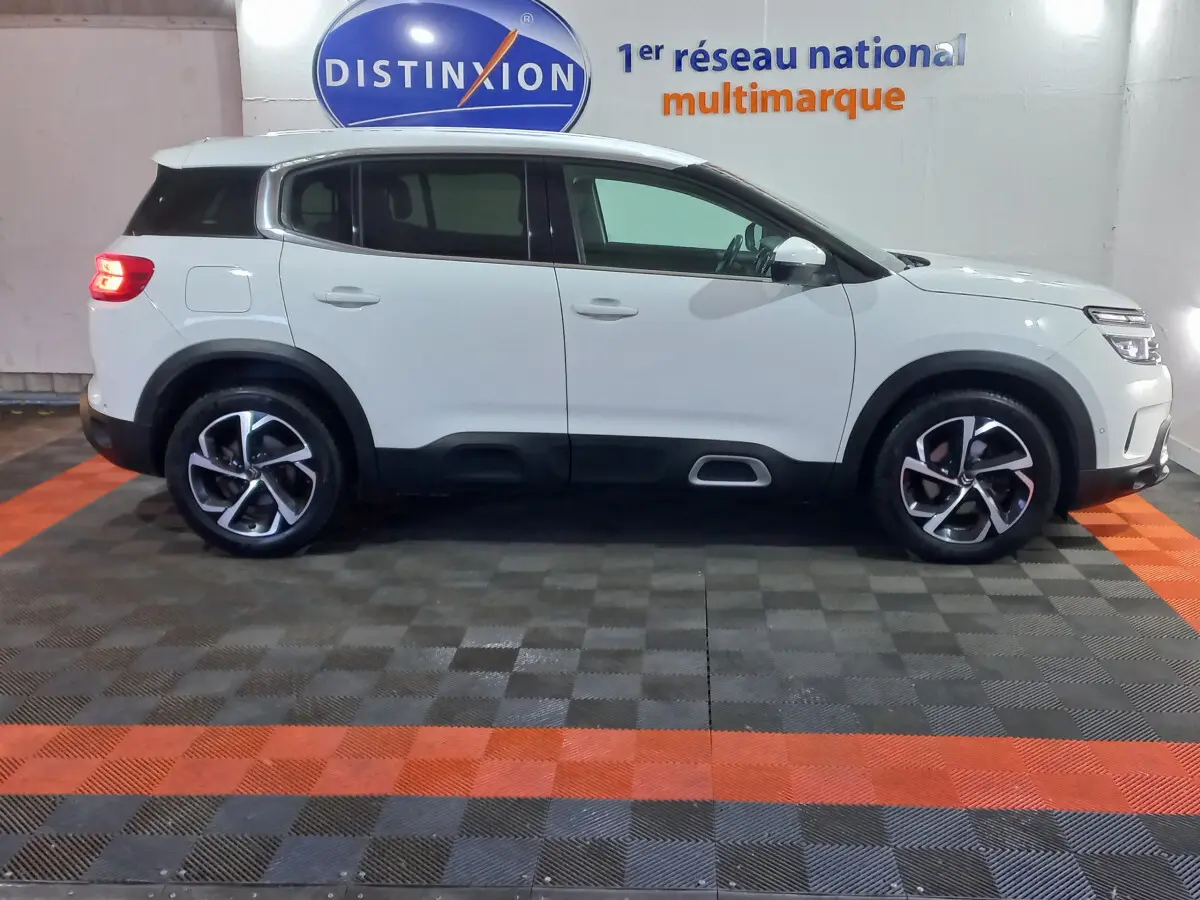 Profil droit d'un SUV Citroën C5 Aircross blanc avec jantes alliage et protections noires basses, en intérieur showroom.