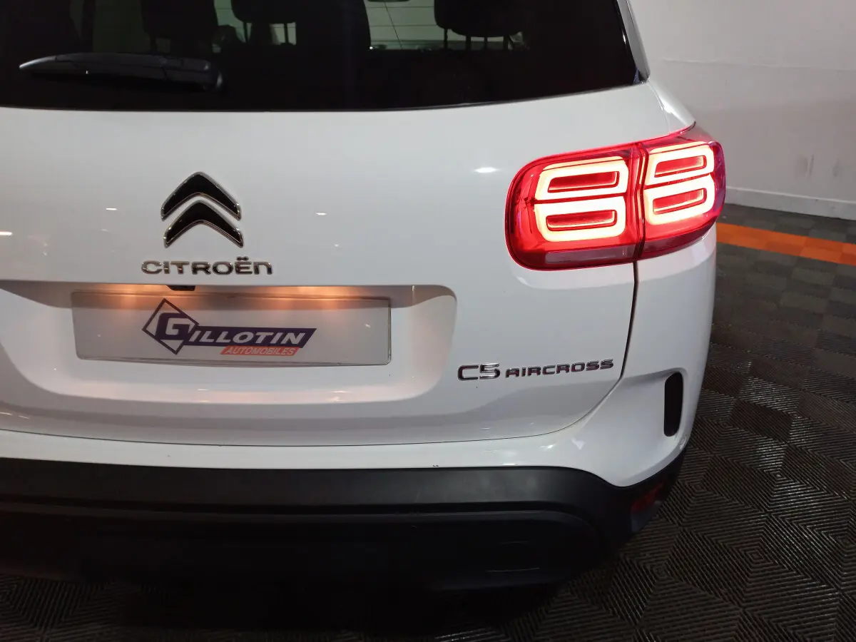 Vue arrière droite d'un Citroën C5 Aircross blanc avec feux arrière LED allumés et logo visible.