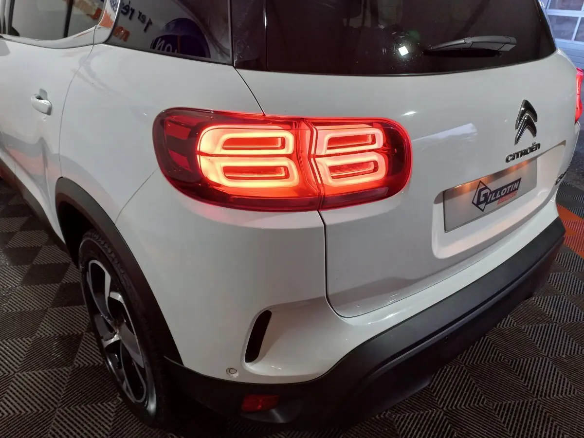 Vue 3/4 arrière droite d'un Citroën C5 Aircross blanc avec feux arrière allumés et jantes noires.