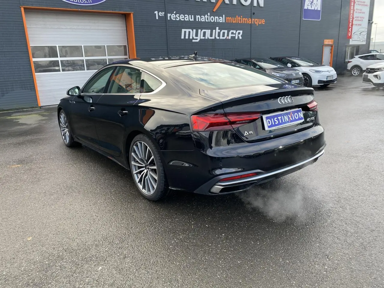 Audi A5 Sportback noir mythic métallisé vue 3/4 arrière droit, avec jantes multibranches et feux LED distinctifs.