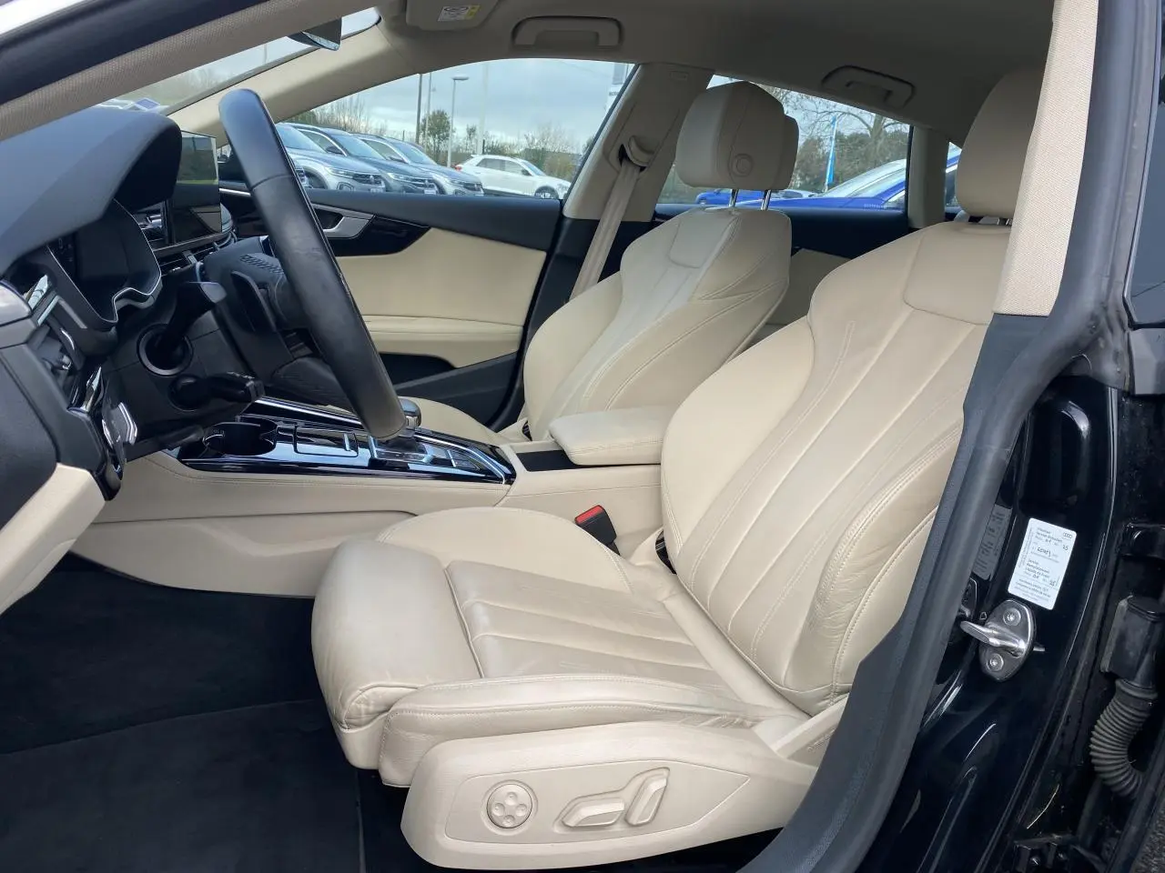 Intérieur côté conducteur d’Audi A5 Sportback 2022 noir mythic, sièges sport cuir beige et console centrale brillante noire.